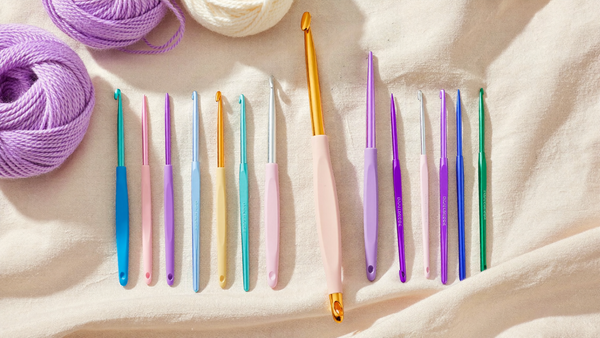 Crochet hook sizes explained — pastel crochet hooks arranged by size on cream linen with yarn