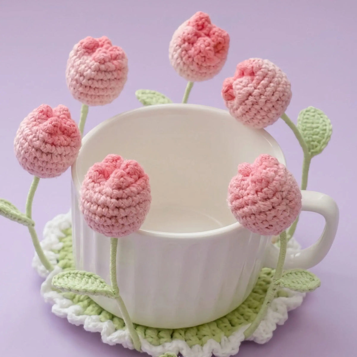 Pink ball-flower crochet coaster with stems hugging a white mug