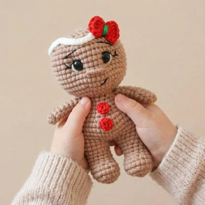Gingerbread crochet pattern: amigurumi gingerbread girl with red bow and buttons, held in hands
