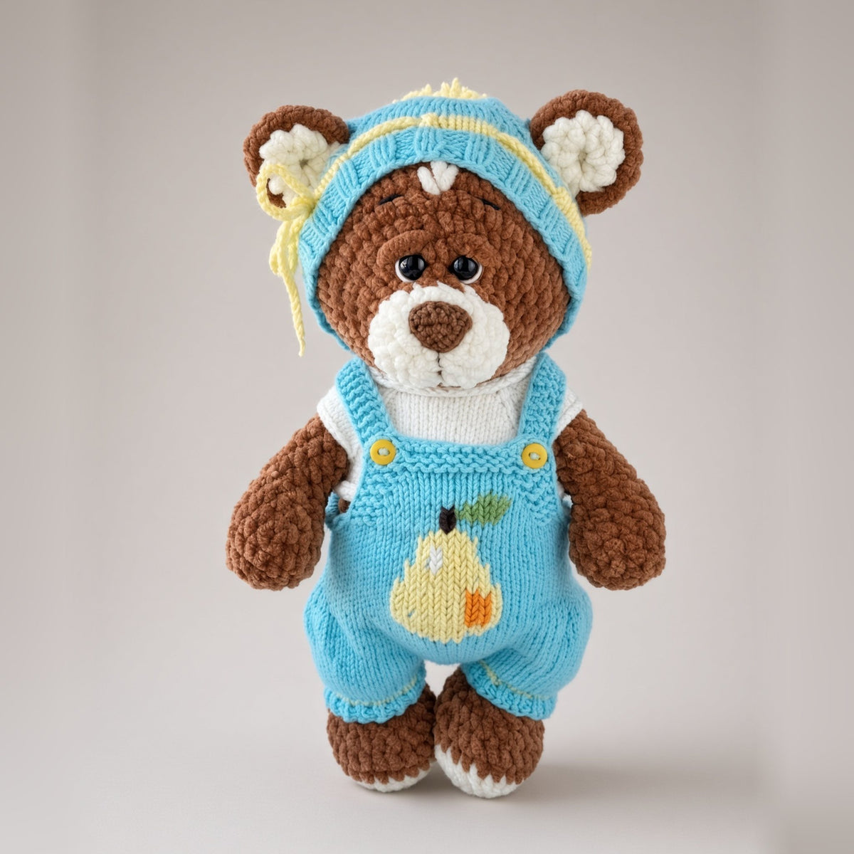 Brownie plush bear in a knitted blue T-shirt, overalls and hat with a pear motif
