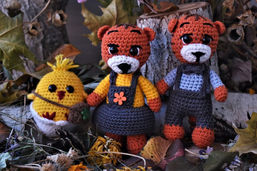 Charming handmade crochet toys pose amidst fallen leaves and tree logs in a cozy autumn scene.